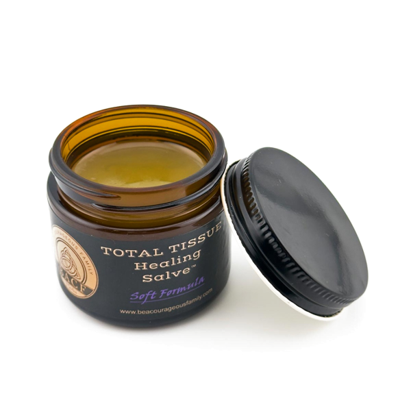 An open amber glass jar of Total Tissue Healing Salve with its black lid resting beside it on a white background.