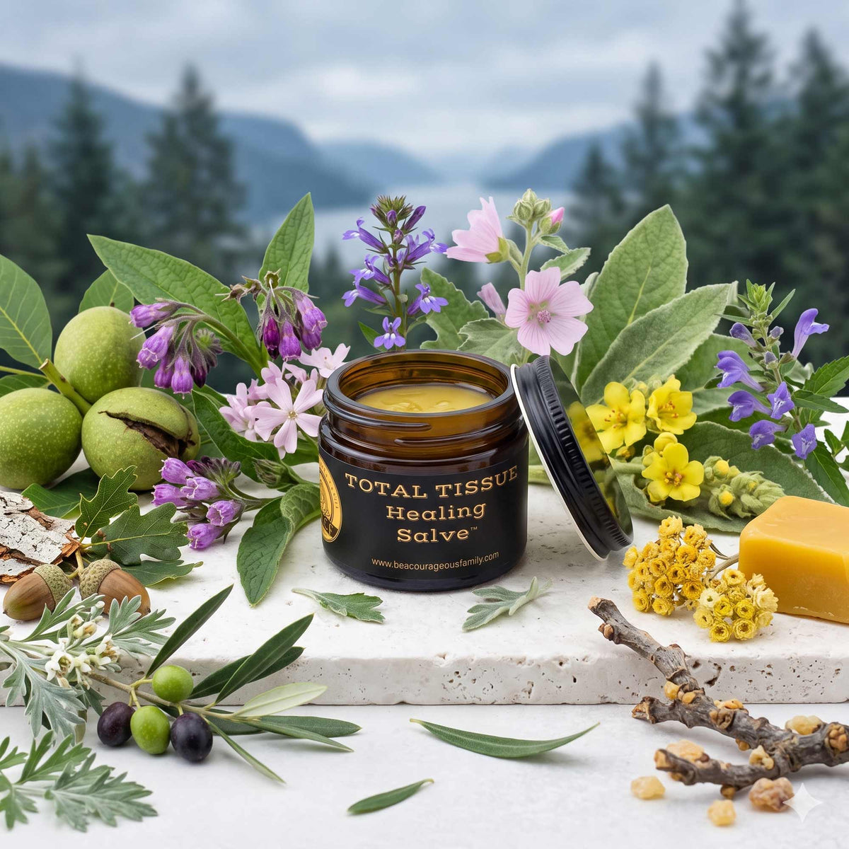 A jar of Total Tissue Healing Salve is displayed on a stone surface surrounded by natural ingredients and flowers, with a blurred forest and mountain background. The amber glass jar contains a yellow balm and has its black lid leaning beside it.